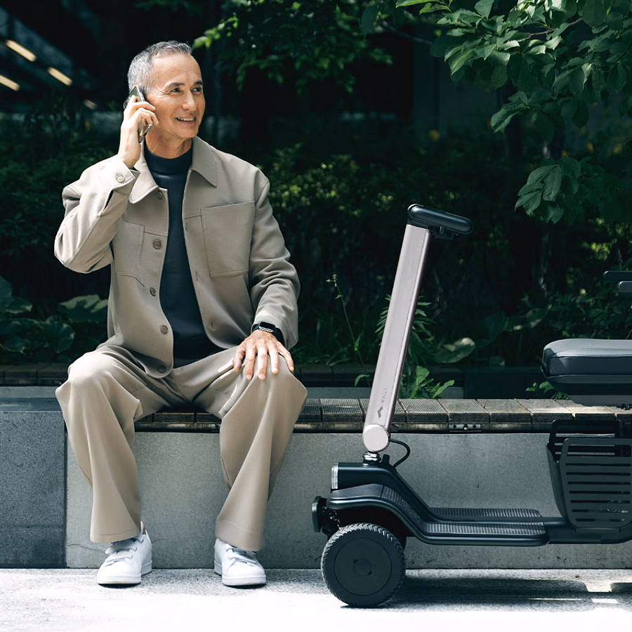 A person talking on phone sitting close to a WHILL model R 4-wheel mobility scooter